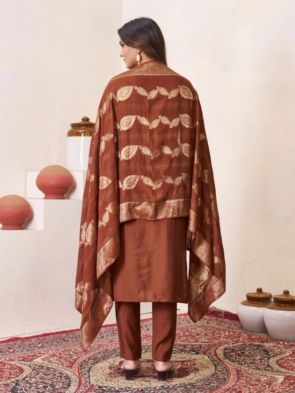 Woman wearing a brown traditional outfit with a patterned shawl in a decorative setting.